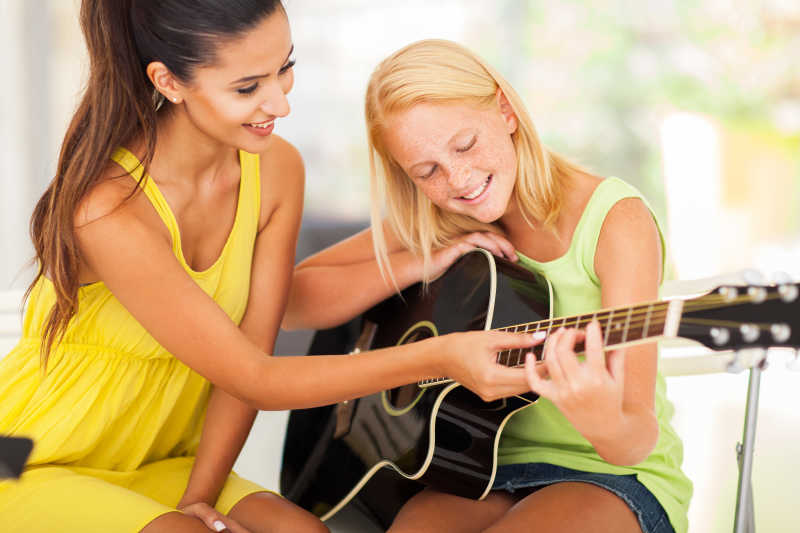 微笑美丽的音乐老师指导小女孩弹吉他
