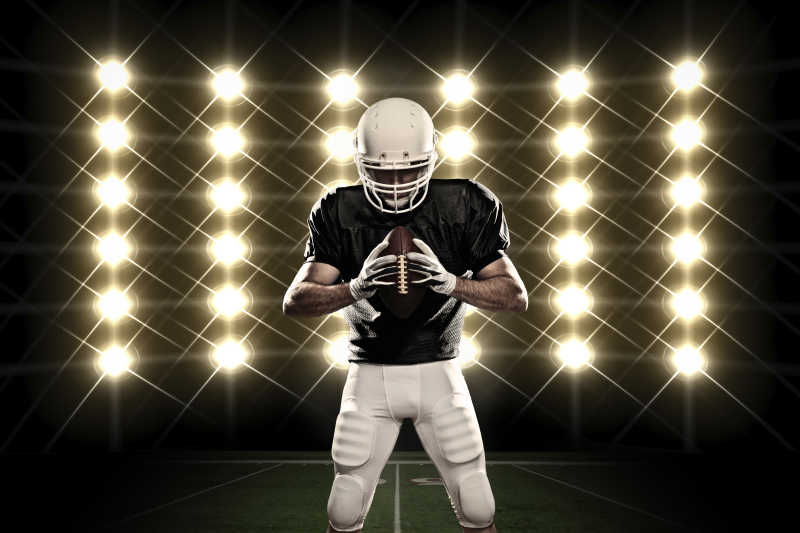在灯光前面有黑色制服的橄榄球运动员