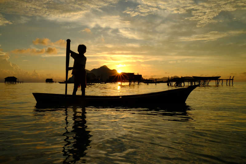 婆罗洲海面撑船的小男孩剪影