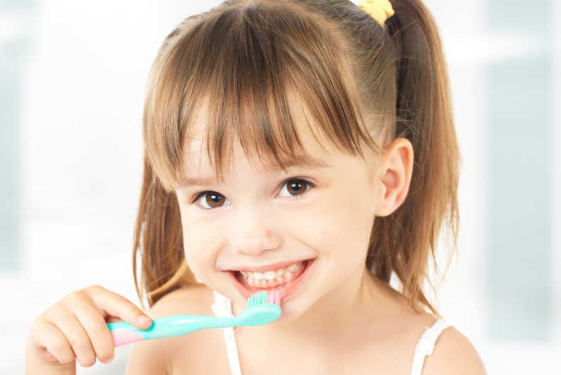 白色背景下可爱的小女孩在拿着牙刷刷牙