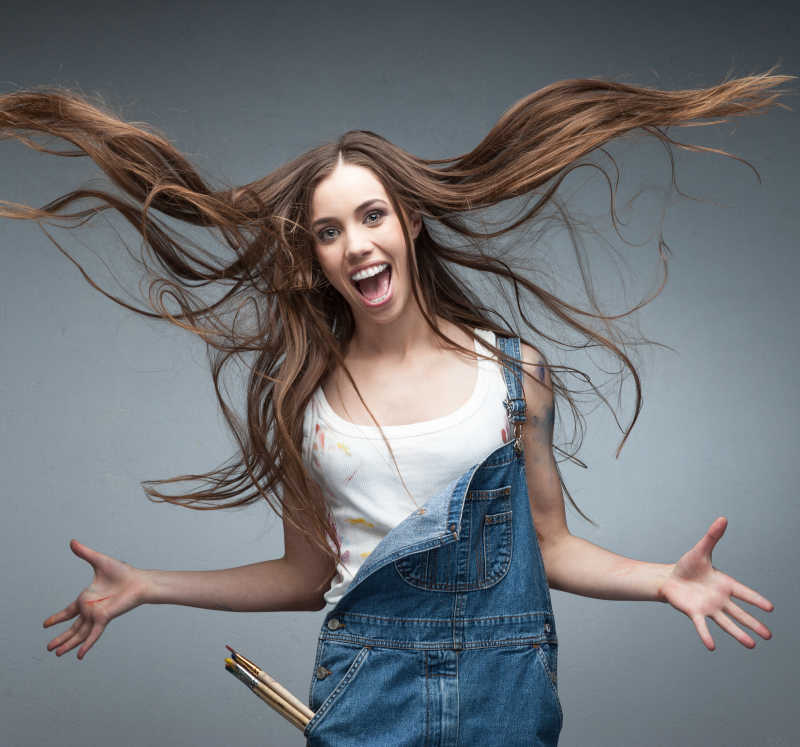 灰白色背景下穿着背带裤头发飞起的开心女人