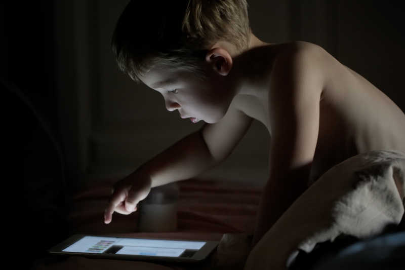 夜间小男孩正在玩平板电脑