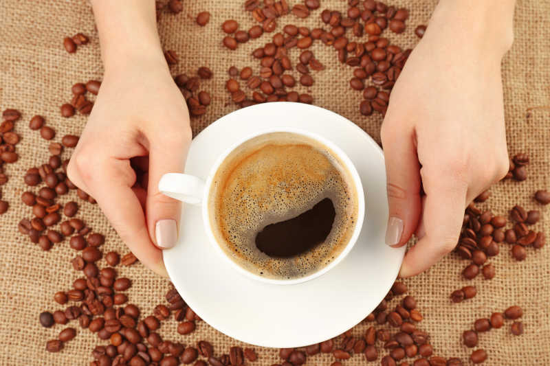 女人端着一杯咖啡在咖啡豆上方