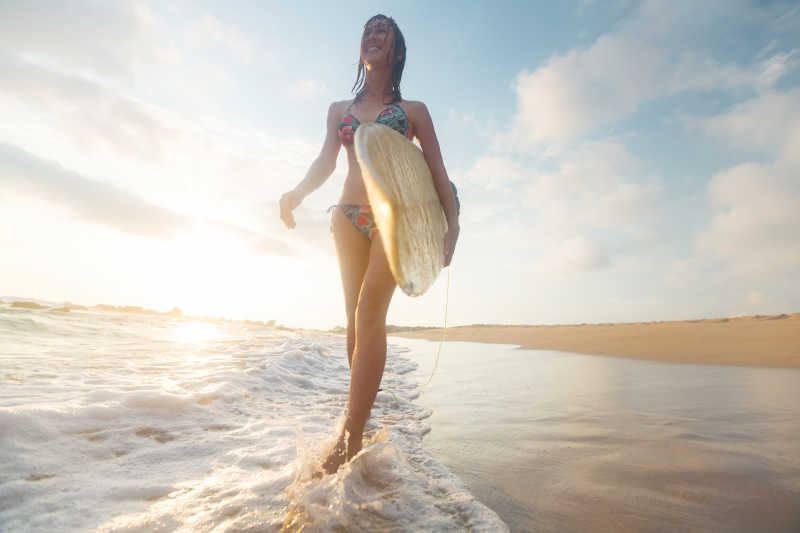 拿着冲浪板在海滩上散步的女孩