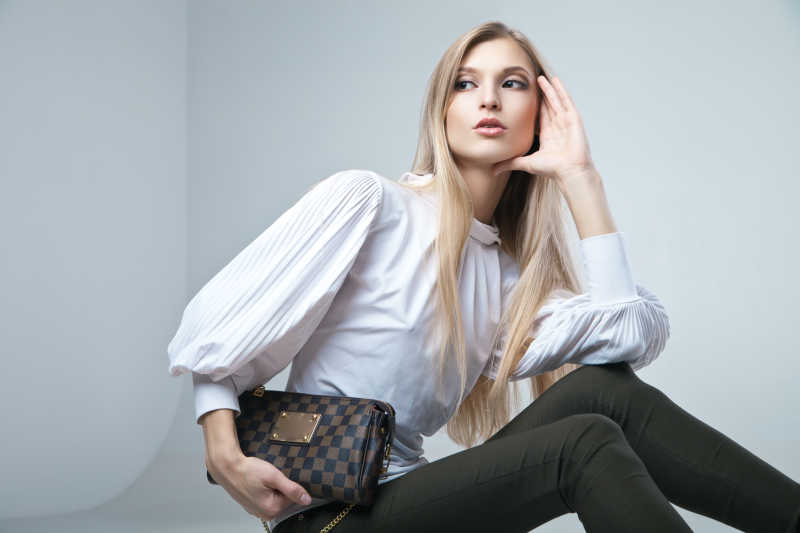 在灯光背景下拿着手提包坐着的美女特写