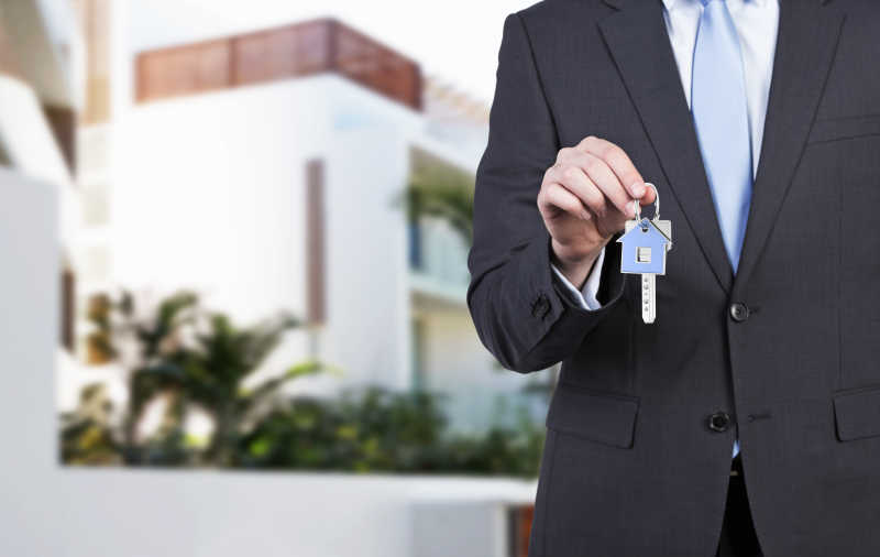 穿西装的男人在房子前展示钥匙