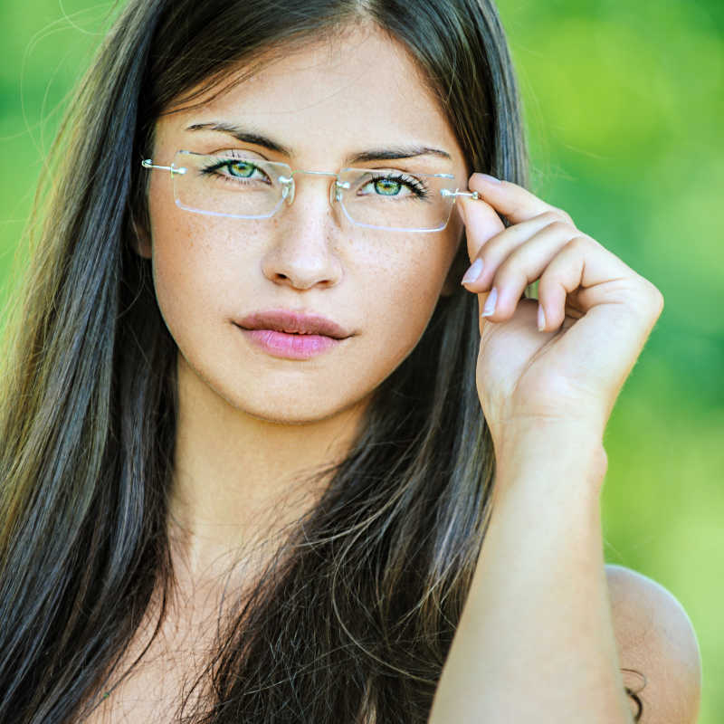 绿色背景下的年轻美女用手指托着无框眼镜
