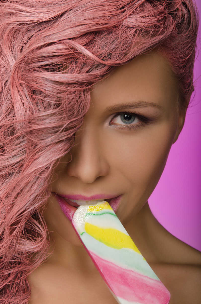 粉色头发的年轻美女正在吃手里拿着的彩色糖果
