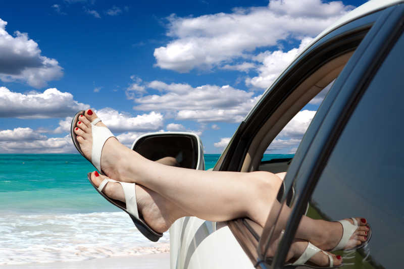 在蓝天大海的背景下女孩将双脚伸出汽车窗外