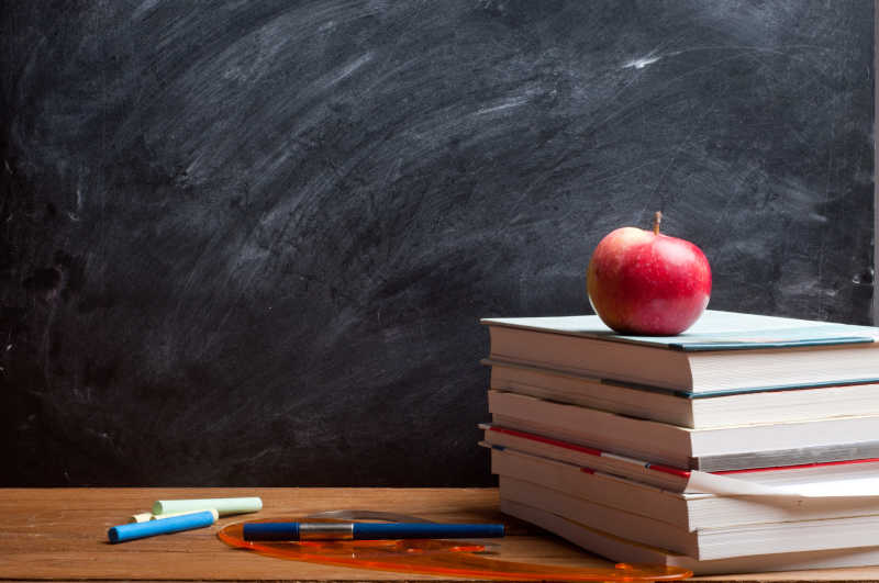 黑板背景下红色的苹果放在教师的书上