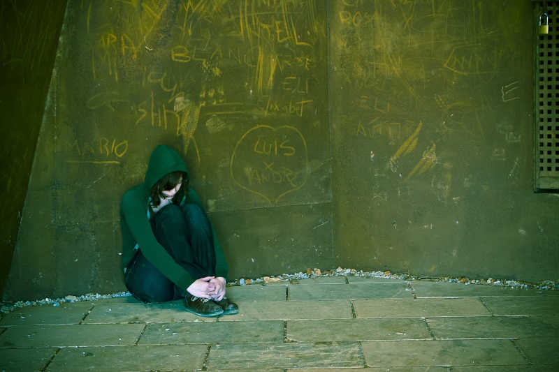 绿色涂鸦墙前抱膝坐在地上的绿衣女子