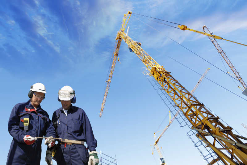 蓝天背景下两个戴安全帽的建筑工人站在起重机下讨论