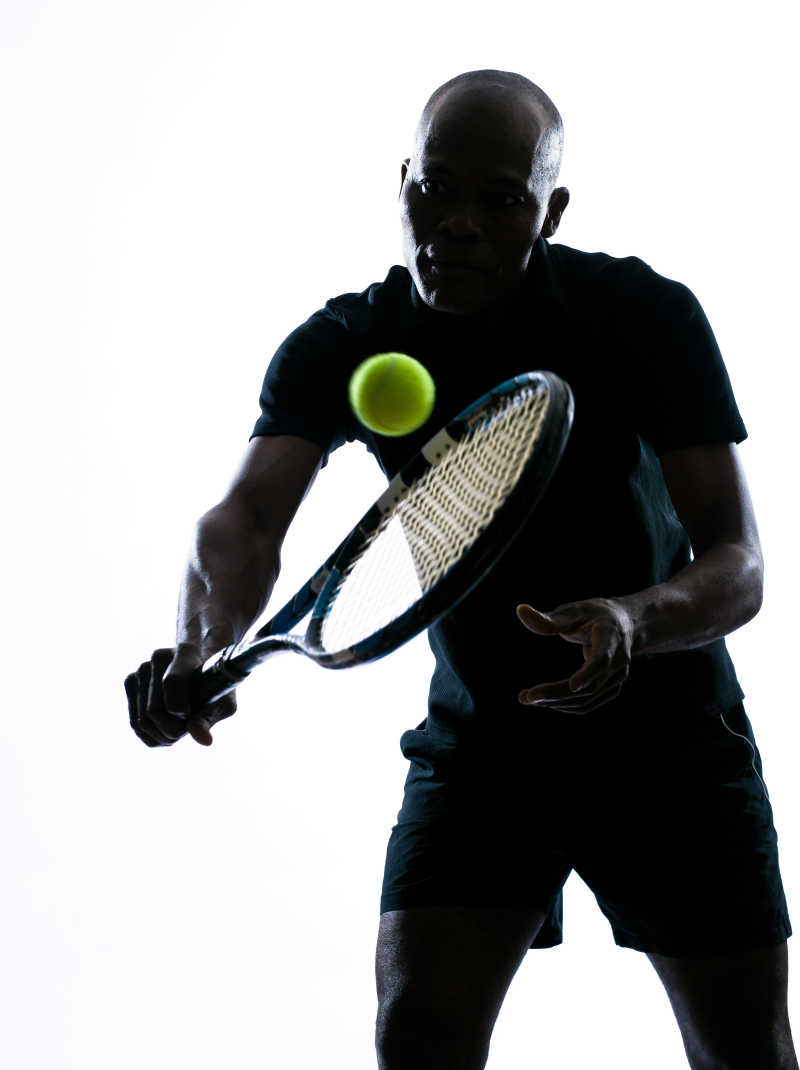 白色背景下非洲裔美国选手拿着网球拍打球