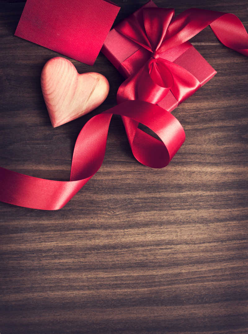 木质桌板上绑着红色丝带的礼品盒和木质红心