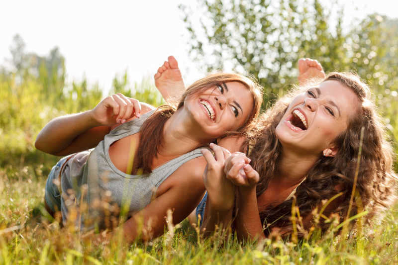 两个穿T恤衫的女朋友在草地上开心的笑