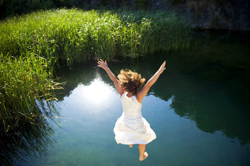 穿着白色连衣裙的年轻女子跳进一个田园诗般的湖泊
