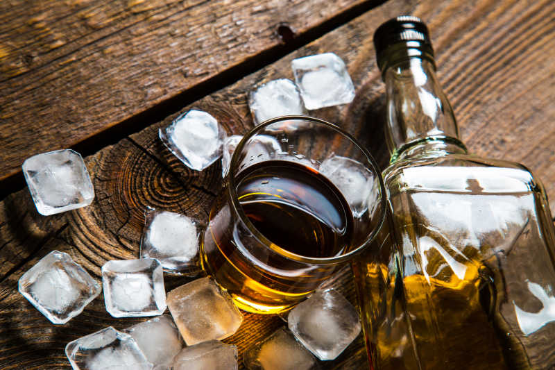 在木桌上的威士忌和冰块