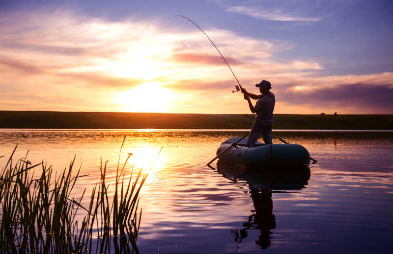 日落下站在皮艇上拿着鱼竿钓鱼的男人