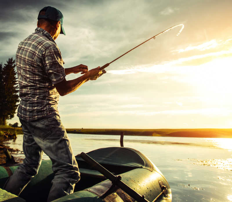 日落时在皮艇上钓鱼的男人