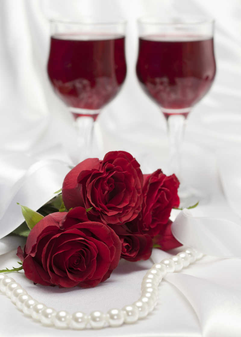 白绸缎上的玫瑰项链和红酒