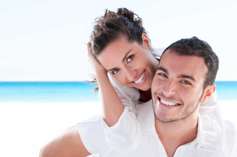 微笑的年轻夫妇在美丽的夏日海滩上