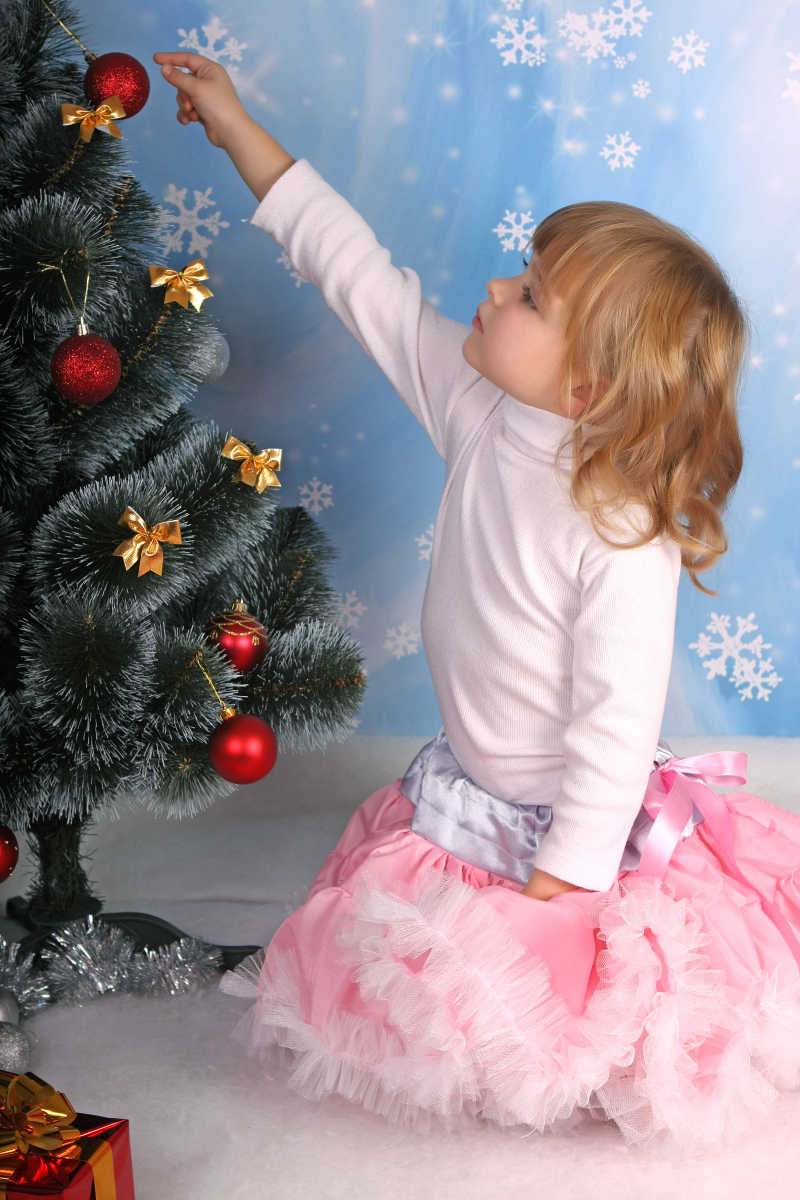 美丽的小女孩玩圣诞树上的装饰球
