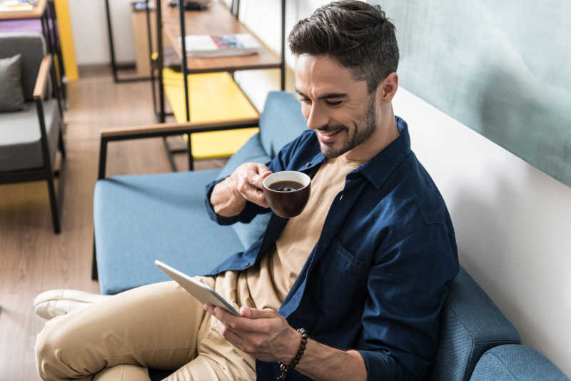 男人做在沙发上喝咖啡看着平板