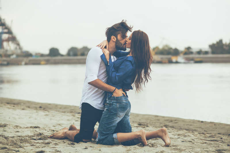 跪在沙滩上亲吻的年轻情侣