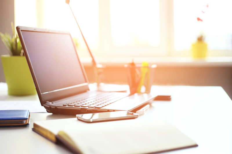 阳光照在桌子上的笔记本电脑和手机上