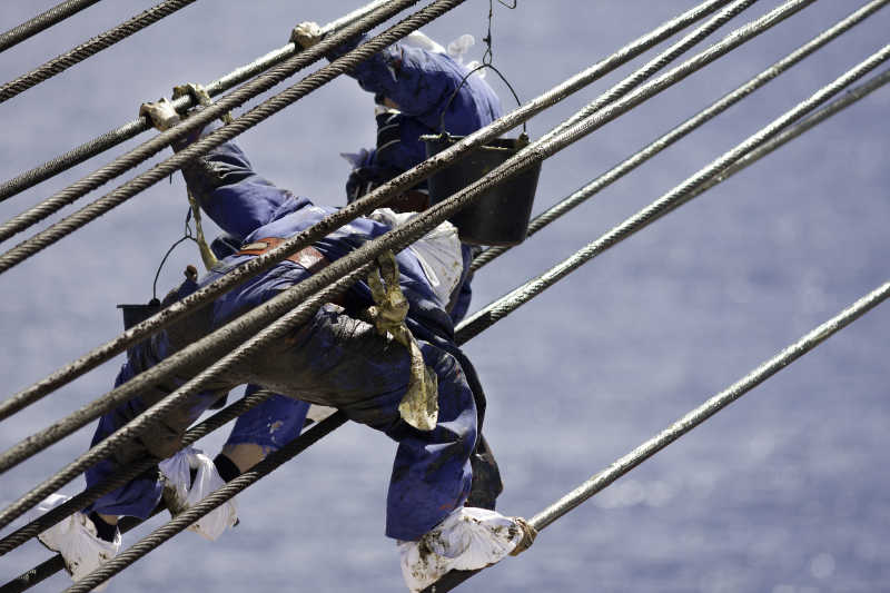 穿着防滑鞋套的工人在润滑钢丝的起重机上工作