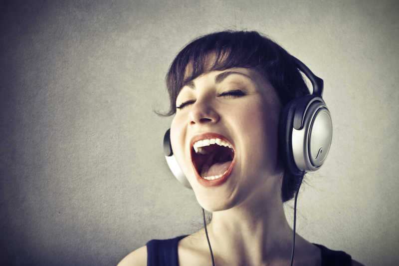 灰色背景下戴着耳机音乐演唱的女人