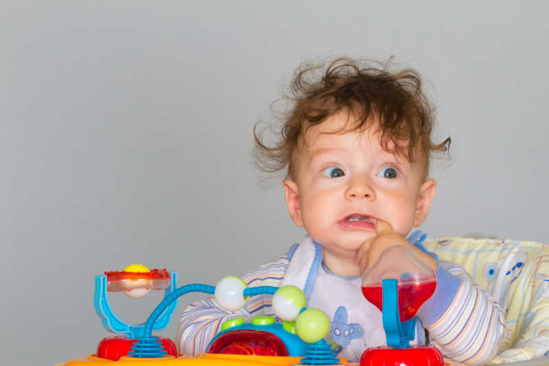 可爱的女婴坐在学步车里叼着手指