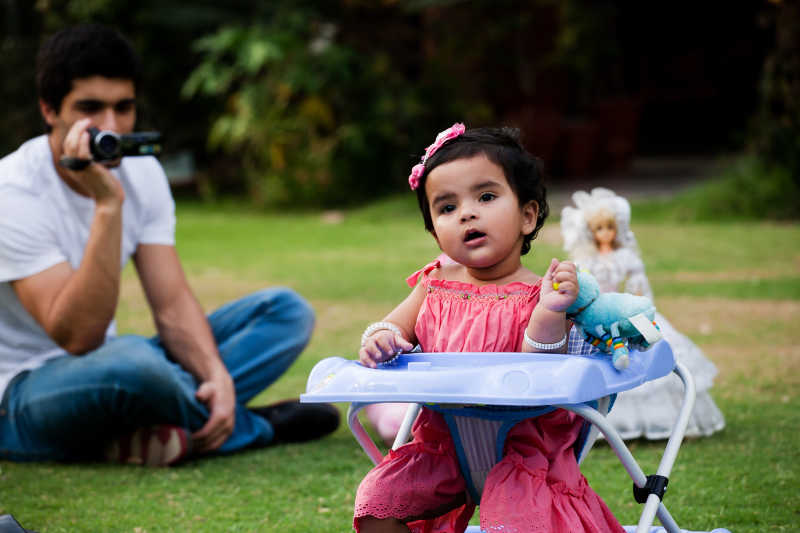 父亲在阳光明媚的下午给坐在学步车的女儿拍照