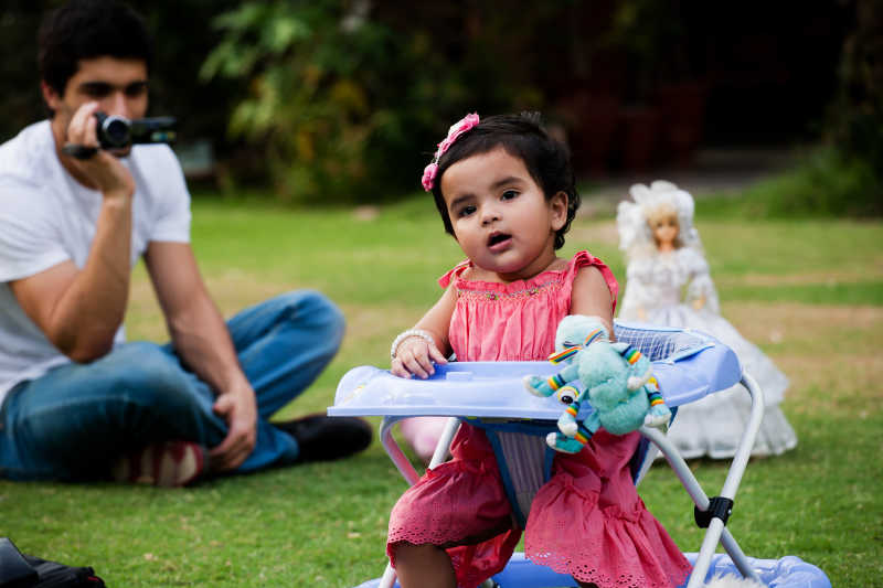 爸爸在给坐在学步车里的女婴拍照