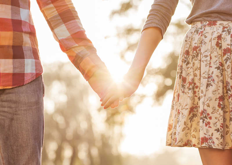 相爱的年轻情侣漫步在秋日的公园里手牵着走手在夕阳中