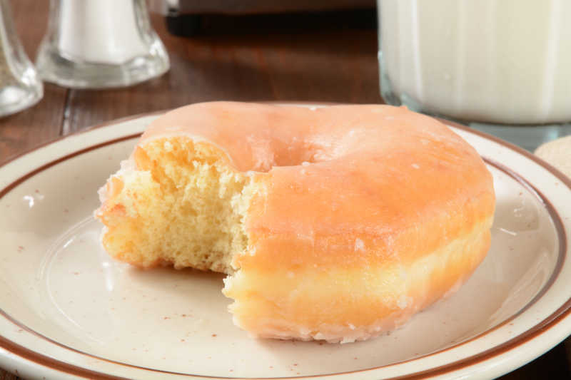 木桌上白色盘子里的甜甜圈和牛奶早餐