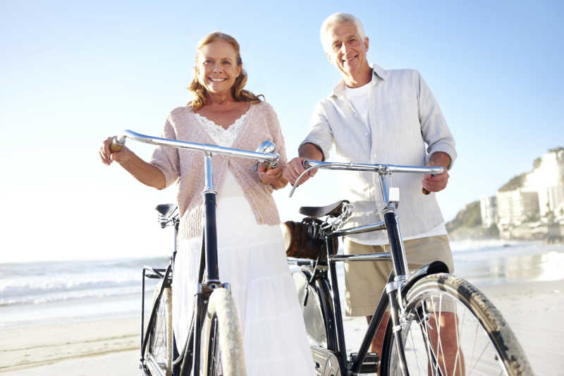 幸福的老夫妇在沙滩上骑自行车