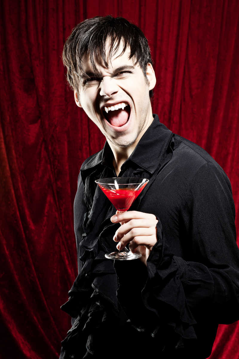 露着尖牙的万圣节吸血鬼拿着一杯红色饮料
