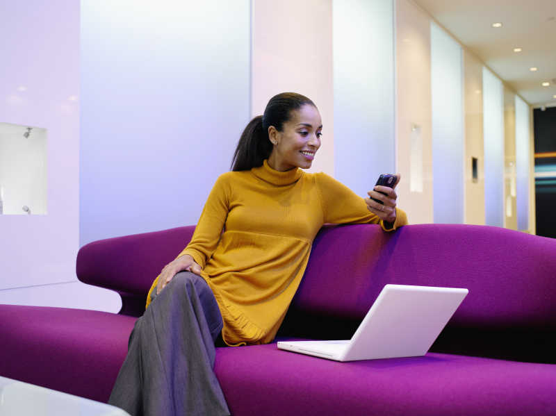 沙发上的笔记本电脑和看着手机的女商人