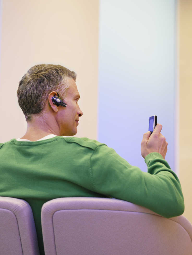 戴着蓝牙耳机看着手机的商人