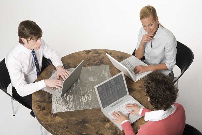 看着笔记本电脑讨论的三个商人