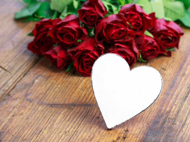 白色心型卡片后面放着殷红色的玫瑰花