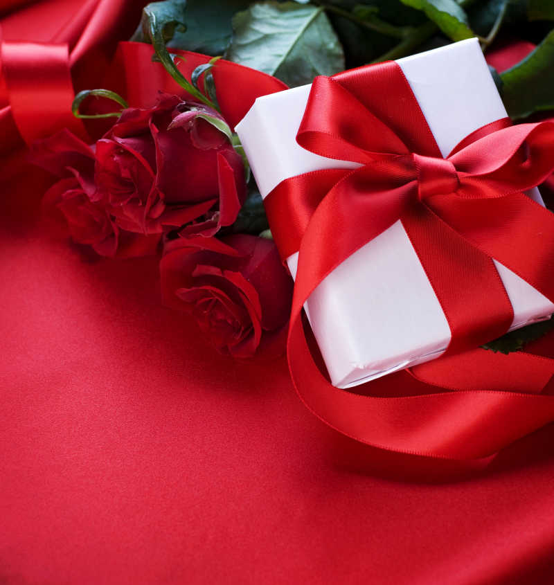 红色绸缎上的玫瑰花和礼品盒