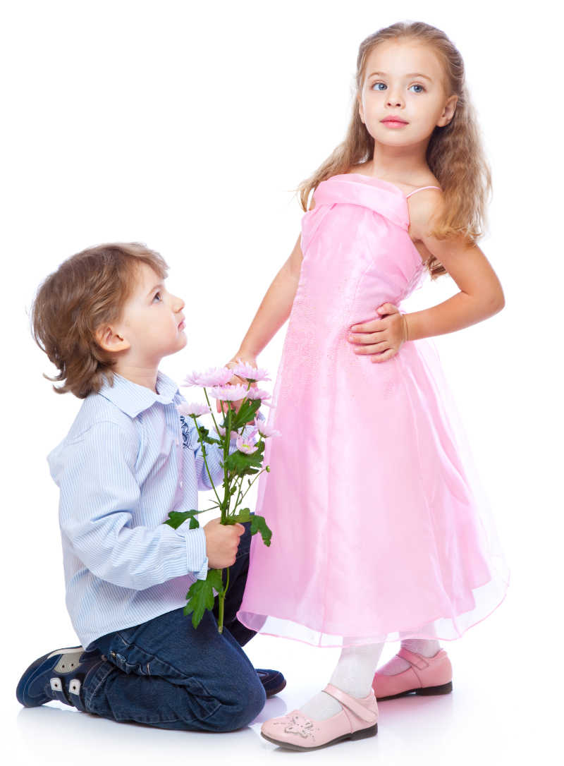白色背景下拿着一束花的男孩子跪在穿着公主裙的小女孩旁边