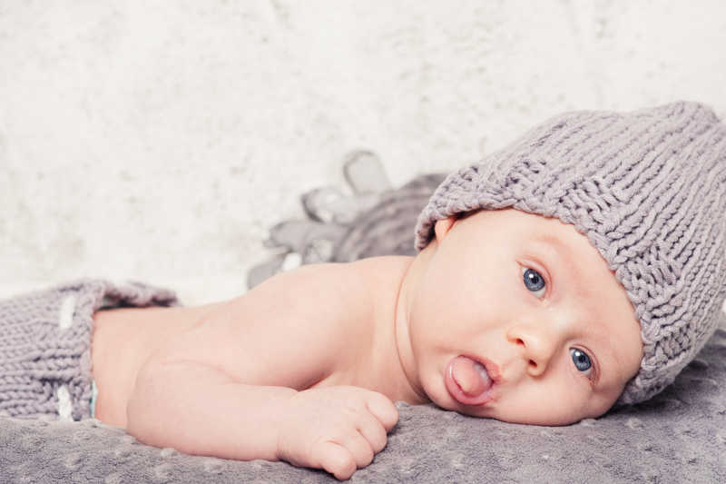 戴着灰色帽子的小男孩躺在灰色的床单上