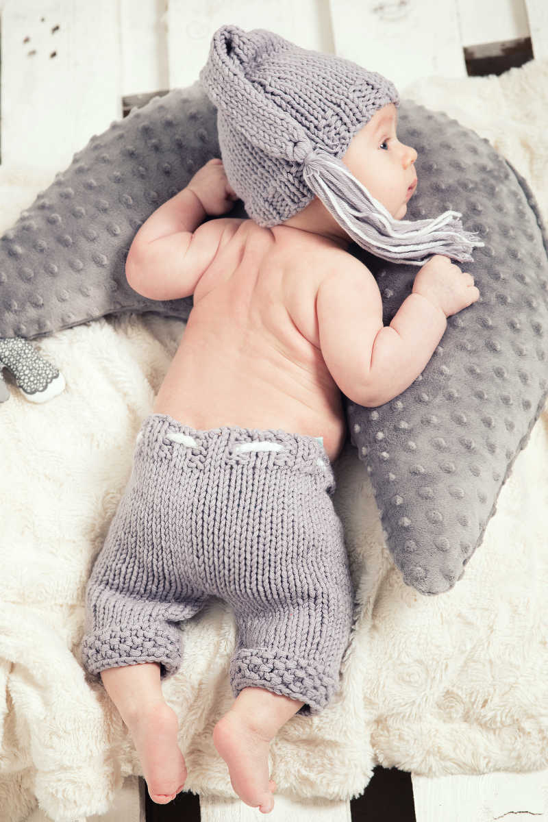 穿灰色针织裤子带灰色针织帽的男孩趴在白色毛毯灰色的抱枕上