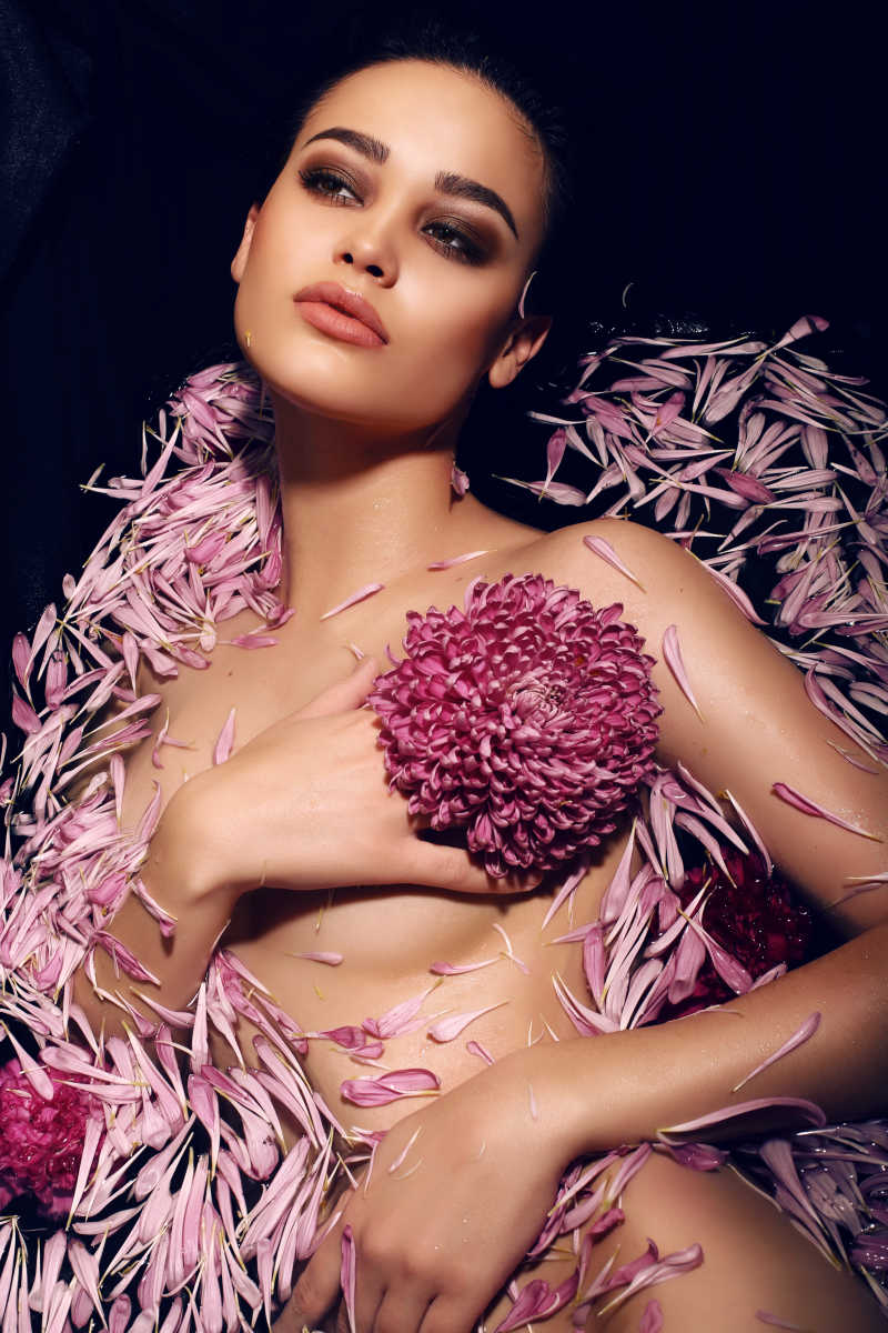 黑色背景下裸体女人躺在飘着菊花的浴缸里