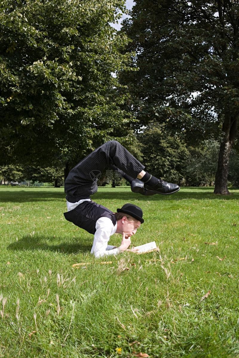 在户外草地上一编练功一边看书的男人