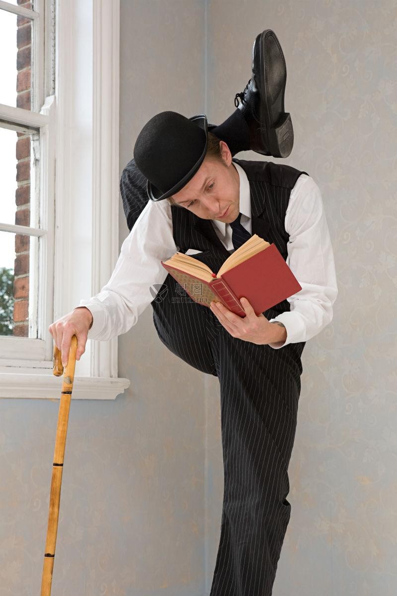 带着圆角礼帽的柔术男演员拿着手杖读一本书