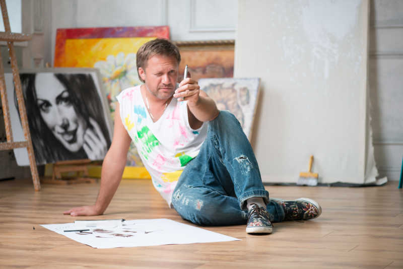 画室地板上坐着一个穿着背心和牛仔裤的男人